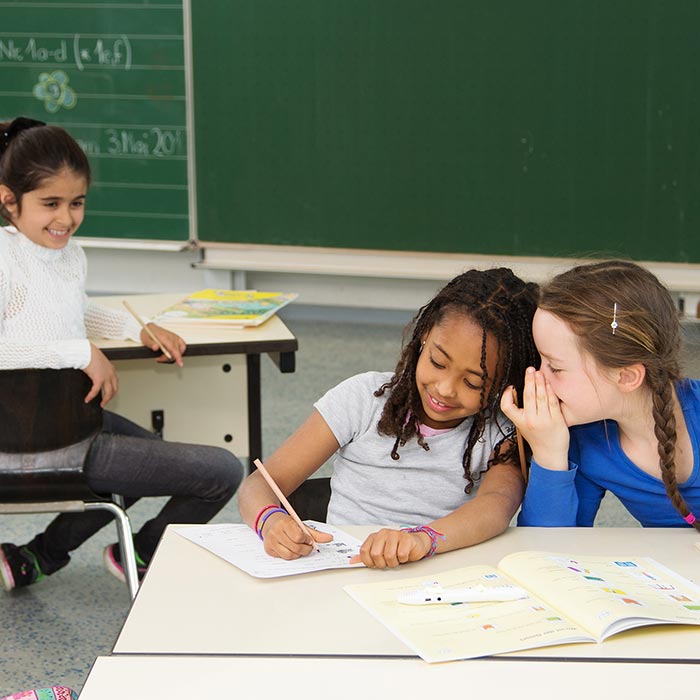 DaZ und Sprachförderung mit "Komm zu Wort!!" Kinder im Klassenraum sitzen am Tisch und bearbeiten die Arbeitsblätter "Komm zur Wort!"
