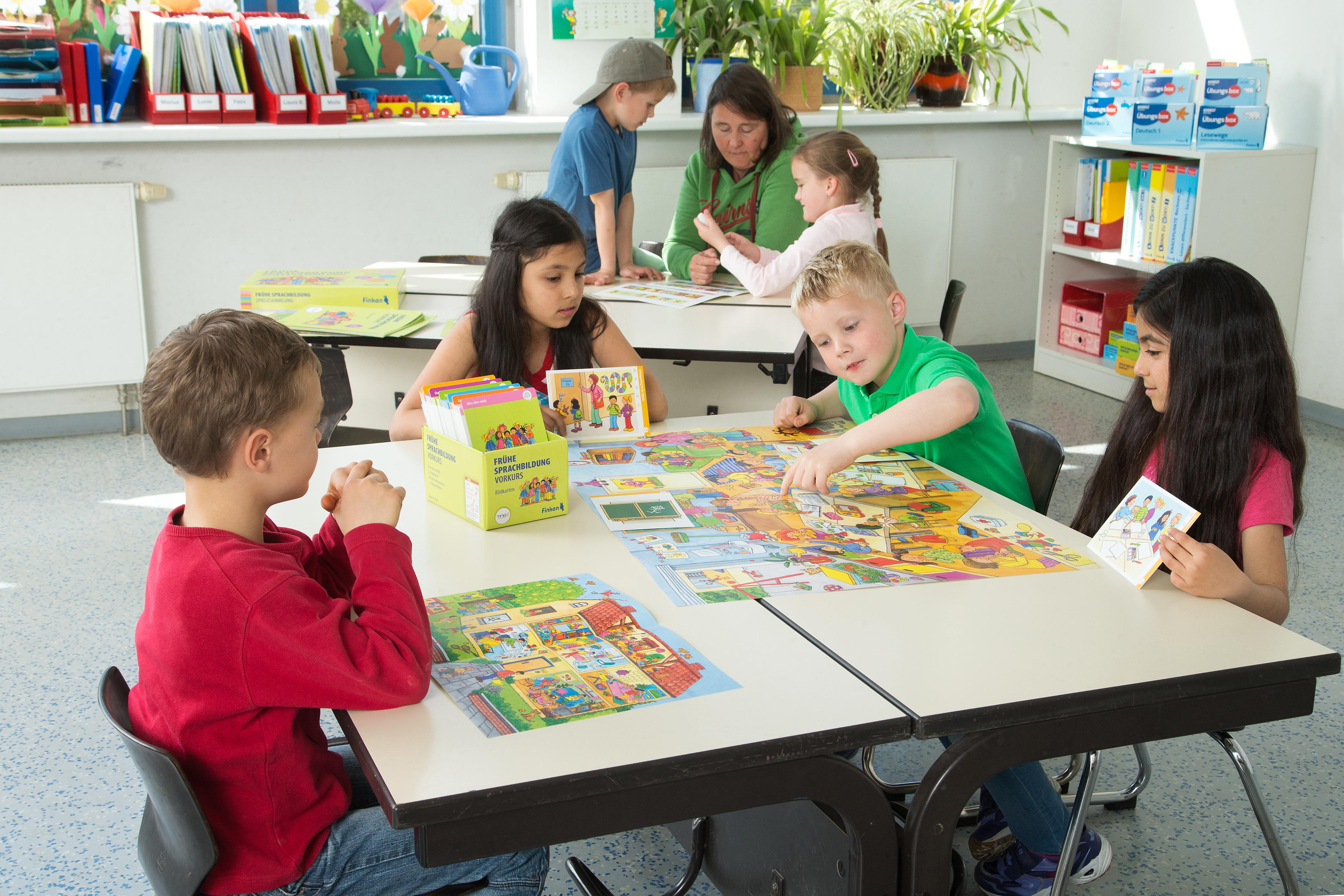 Frühe Sprachbildung Vorkurs in Unterrichtsalltag Kinder und Lehrerin sitzen in einem Klassenraum und arbeiten mit den Materialien aus Frühe Sprachbildung Vorkurs